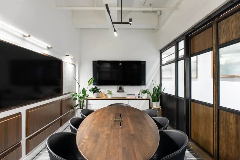 Meeting room with an oval wood table, black chairs and wall-mounted display screen